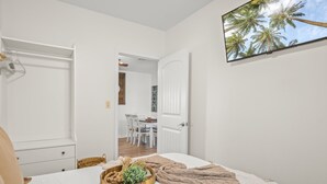 Une chambre à coucher comprenant un lit, une table de chevet, un téléviseur fixé au mur et une porte donnant sur un coin repas.