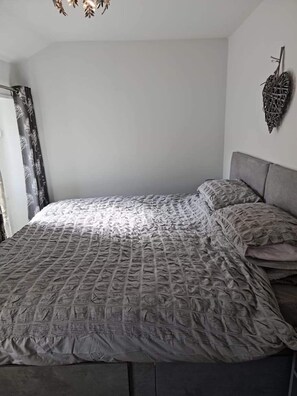 A bedroom with a large bed, a headboard, and a wall-mounted decorative piece. - Charming 2 Bed Cottage in Nidderdale Near Harrogat (Harrogate)