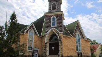 A church with a prominent steeple, stone walls, and large arched windows.