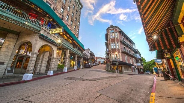 A historic hotel with arched entrances and a classic facade, located in a bustling street with other buildings and shops.