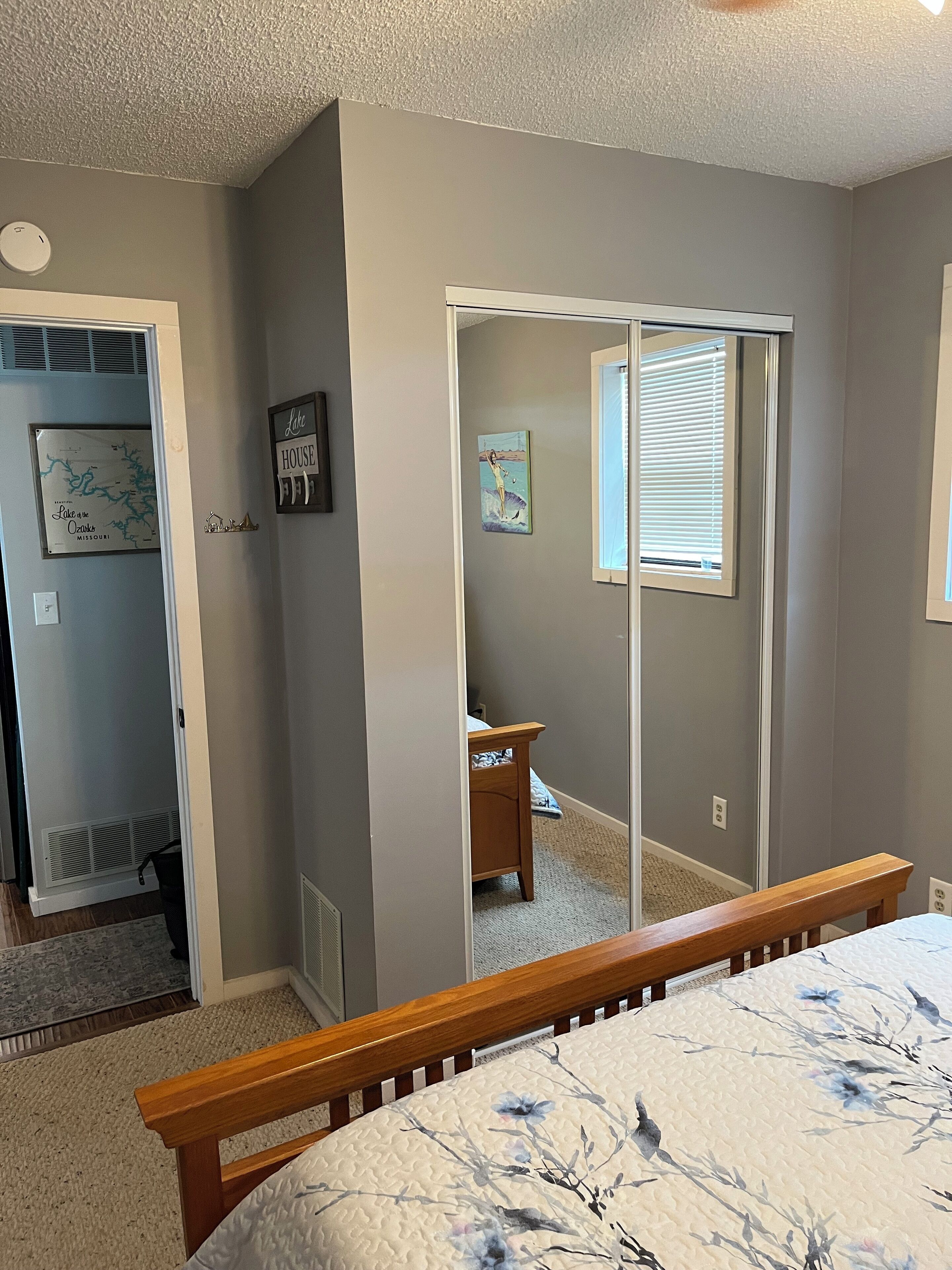 A bedroom with a bed, a wooden bench, a closet with a sliding door, a small table, and a window with blinds.