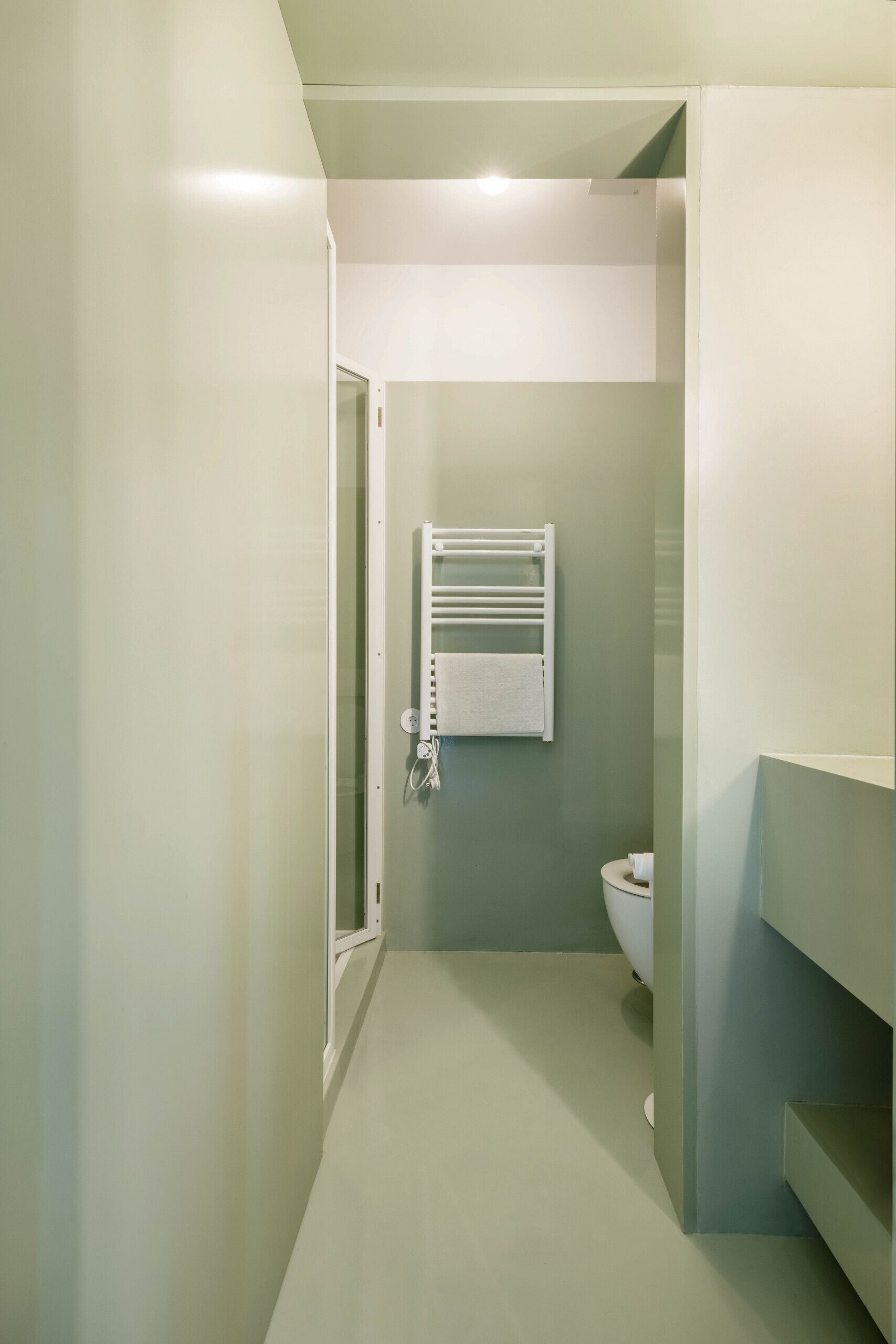 A narrow bathroom with a white bathtub, a towel rack, and a toilet.