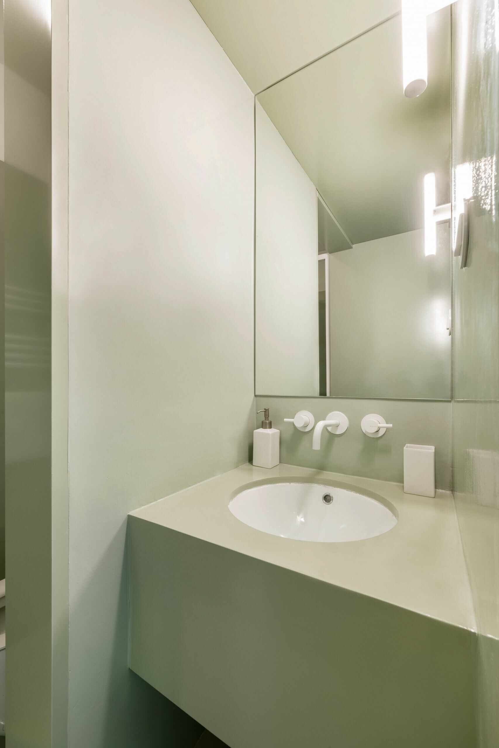 A modern bathroom with a white sink, a large mirror, and a light fixture above the mirror.