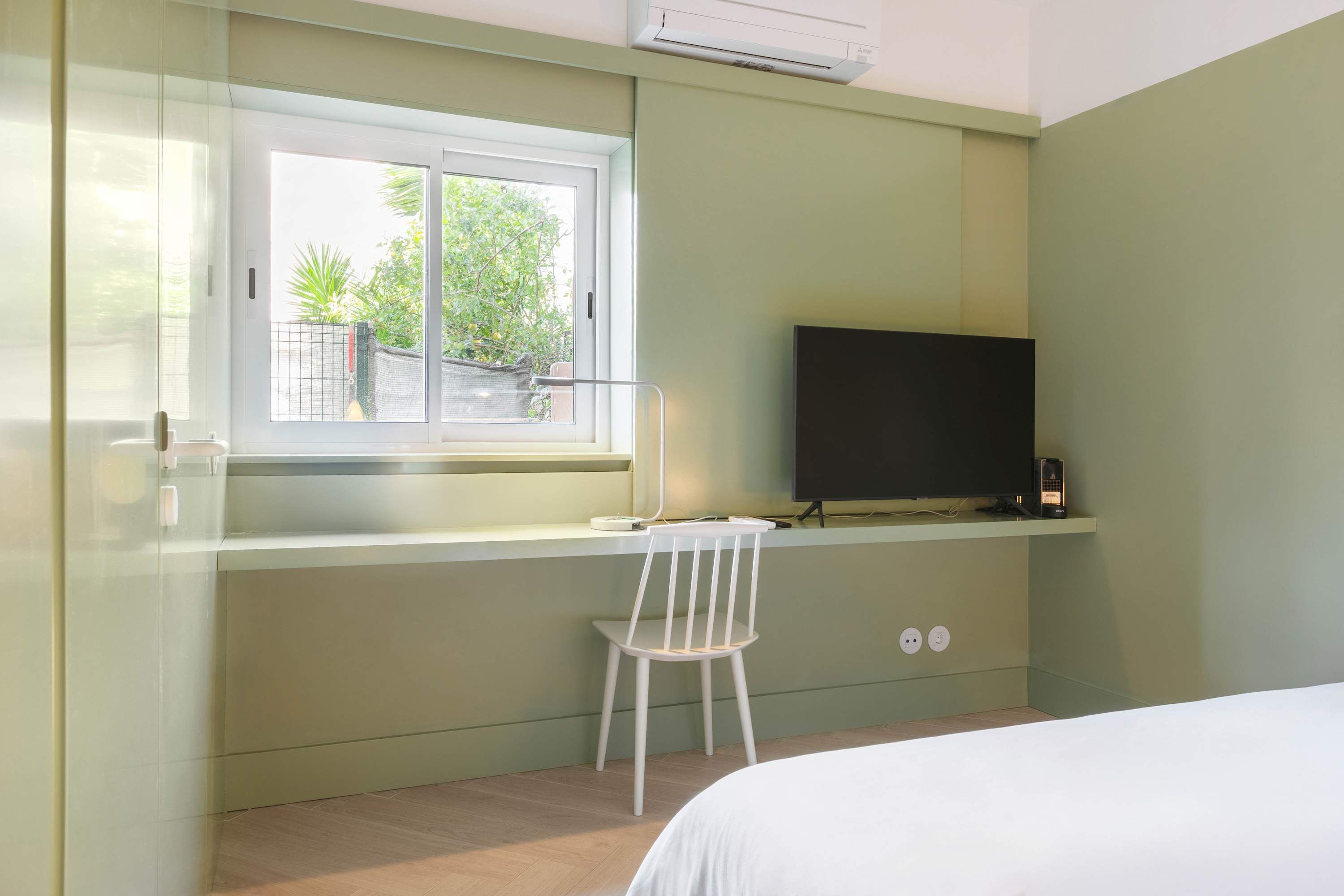 Un dormitorio con cama, ventana, escritorio y silla, y televisor.