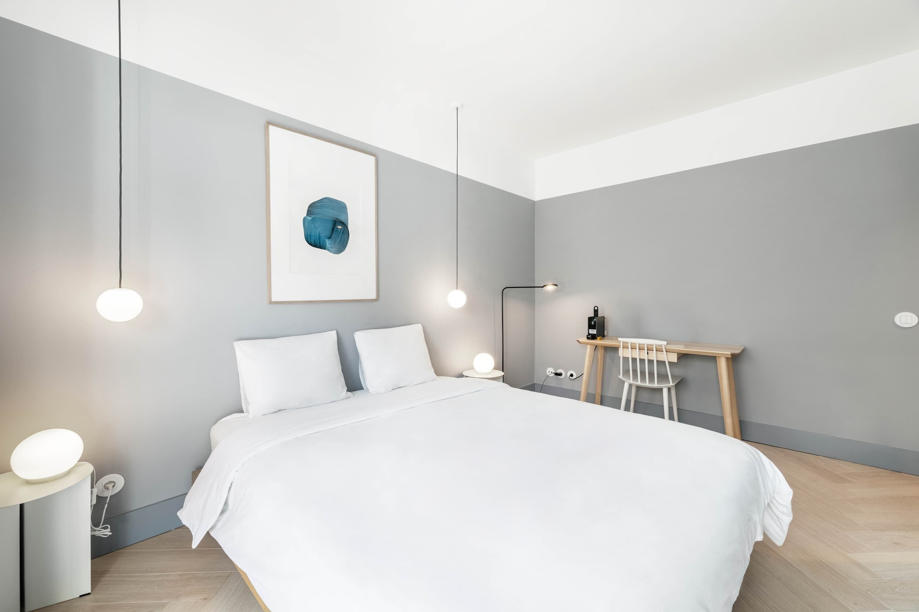 Ein modernes Schlafzimmer mit einem großen Bett, Nachttischen mit Lampen, einem Schreibtisch mit Stuhl und einem gerahmten Kunstwerk an der Wand.