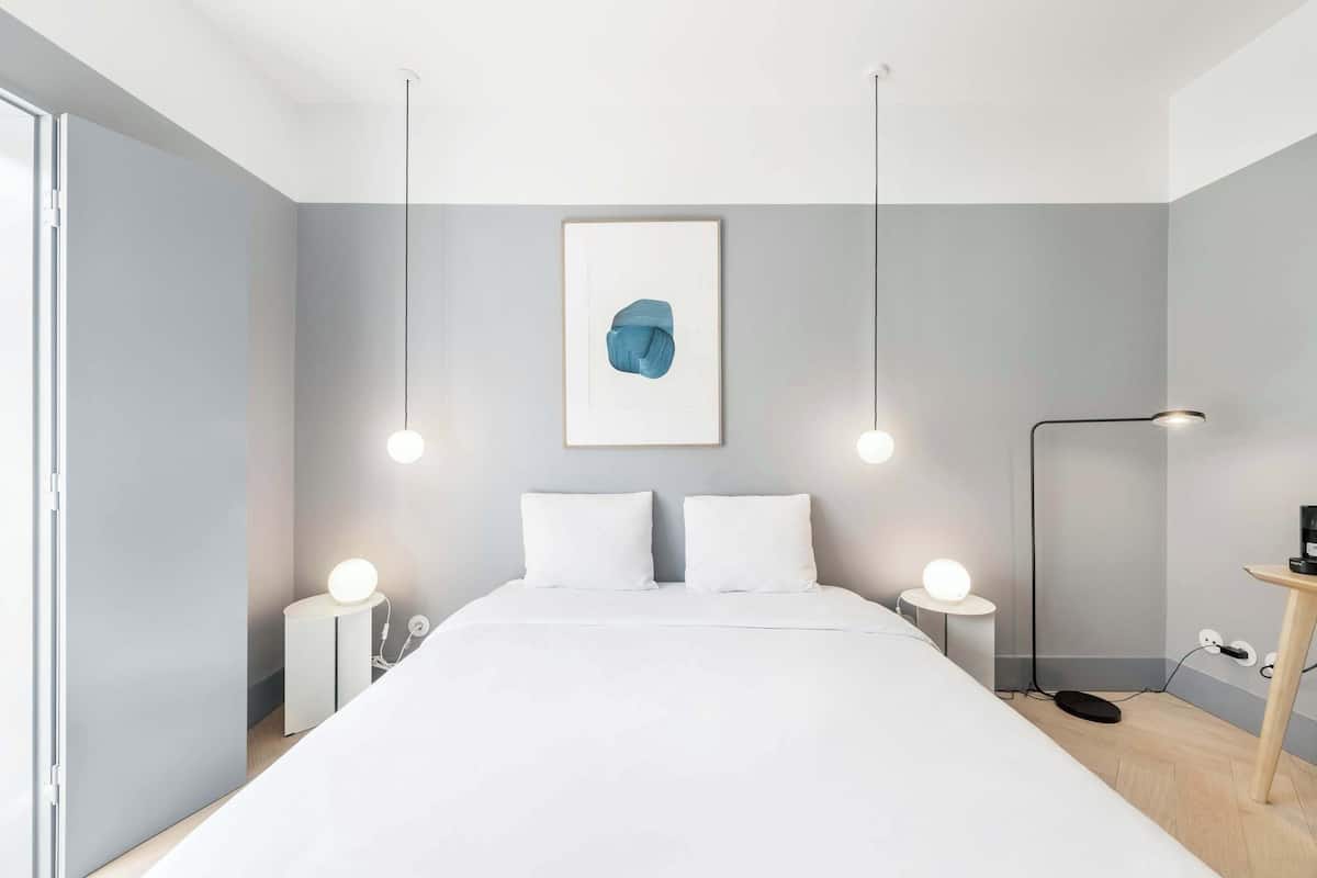 Ein modernes Schlafzimmer mit einem großen Bett, Nachttischen mit Lampen, einer Wandleuchte und einem gerahmten abstrakten Kunstwerk.