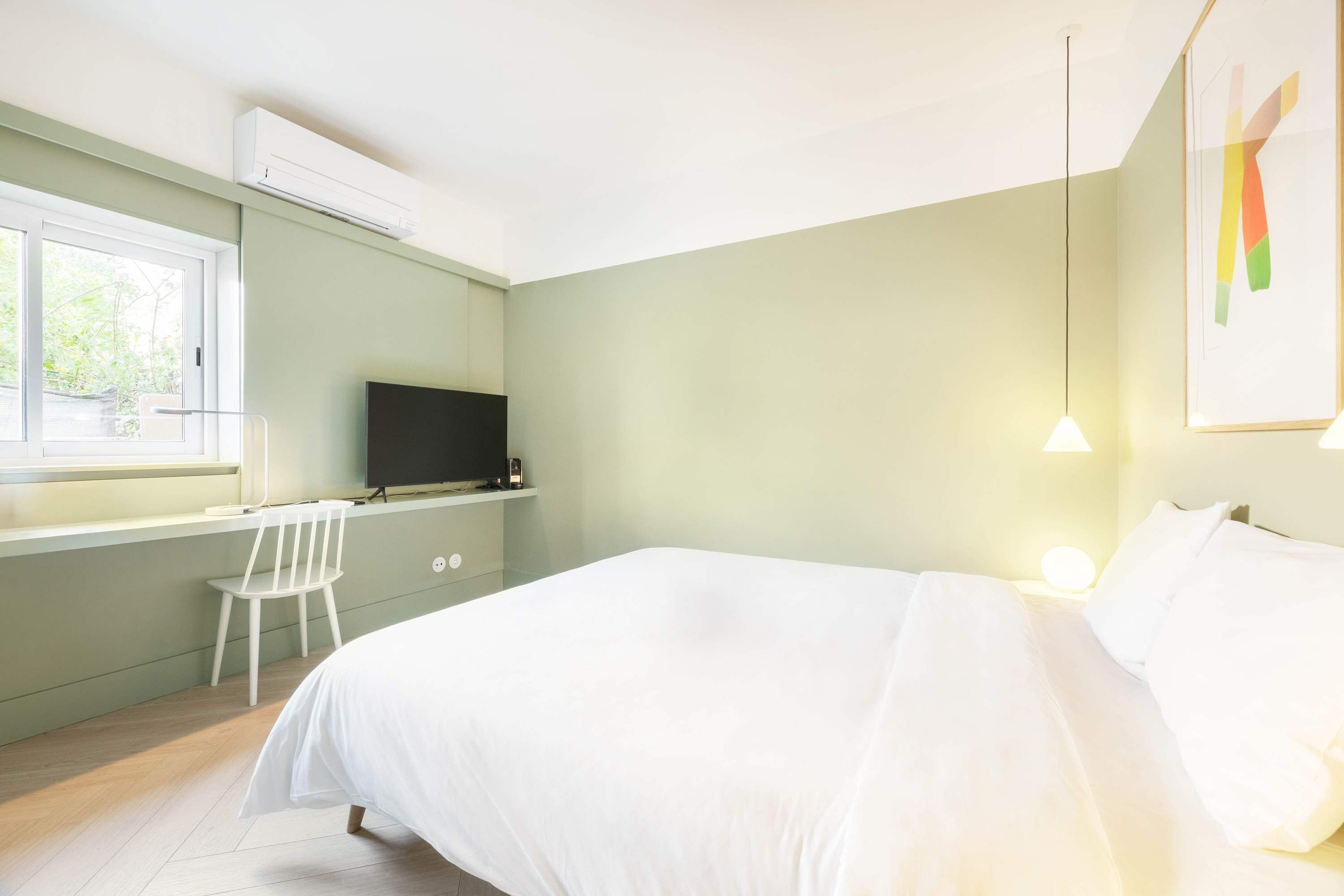 Un dormitorio con cama, escritorio, silla, televisor y ventana.
