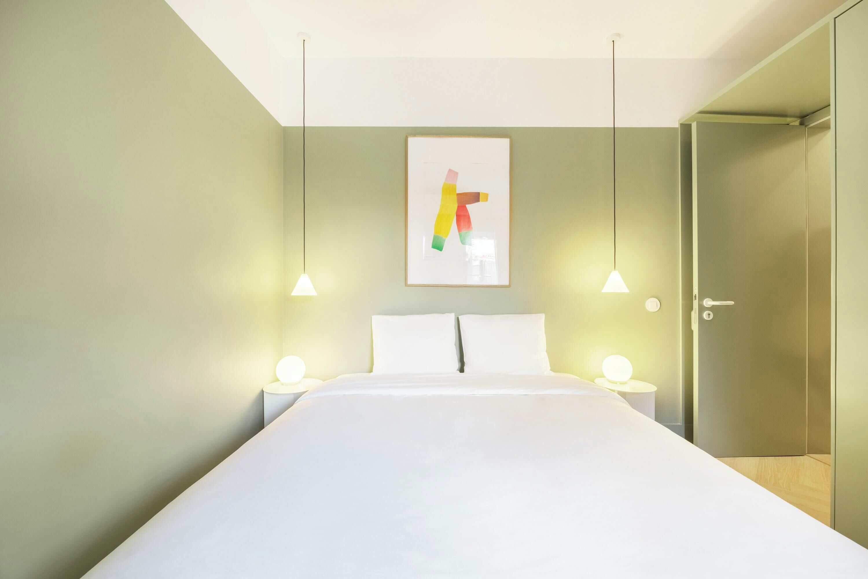 Una camera da letto moderna con un letto grande, due abat-jour, un quadro astratto incorniciato e una porta che dà su una cabina armadio.