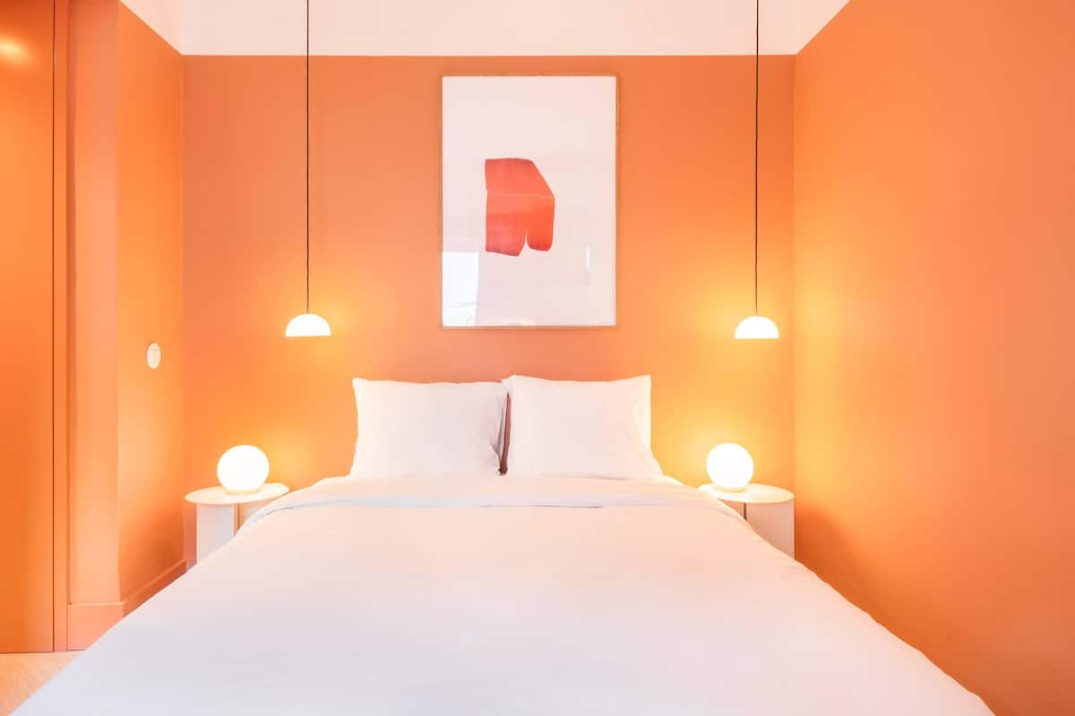 Ein Hotelzimmer mit einem Bett, weißer Bettwäsche, zwei Nachttischen mit Lampen und einem Wandbild.