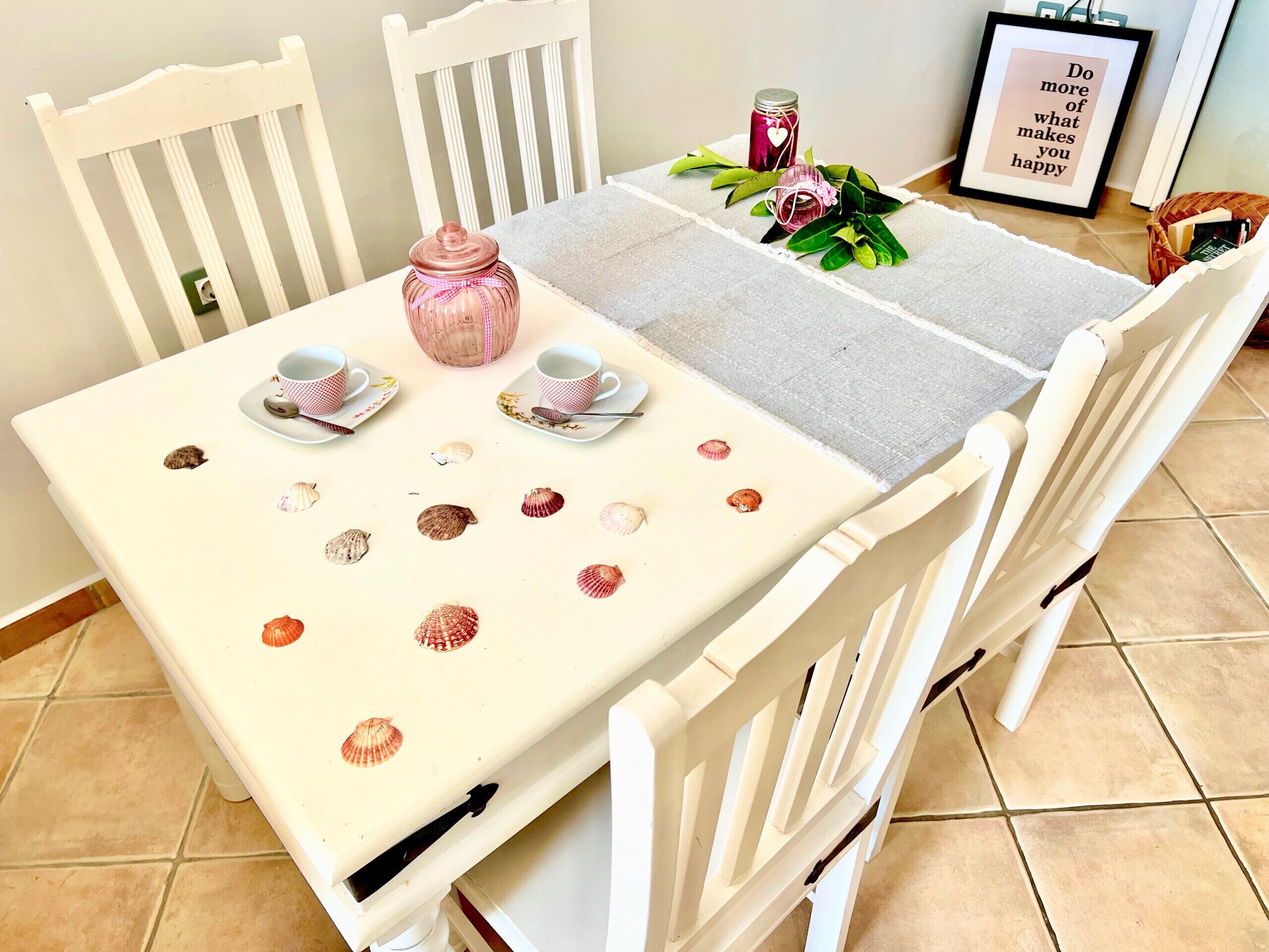 A dining table with a white tablecloth, two cups, saucers, and a pink jar.