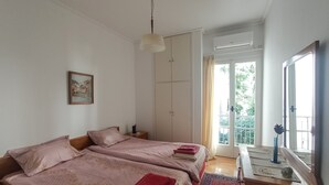 A bedroom with two beds, a dresser, a painting, and a balcony with a view of greenery. - 3-Generations Athenian home at the foot of the Acropolis hill in Athen"s center (Athina)