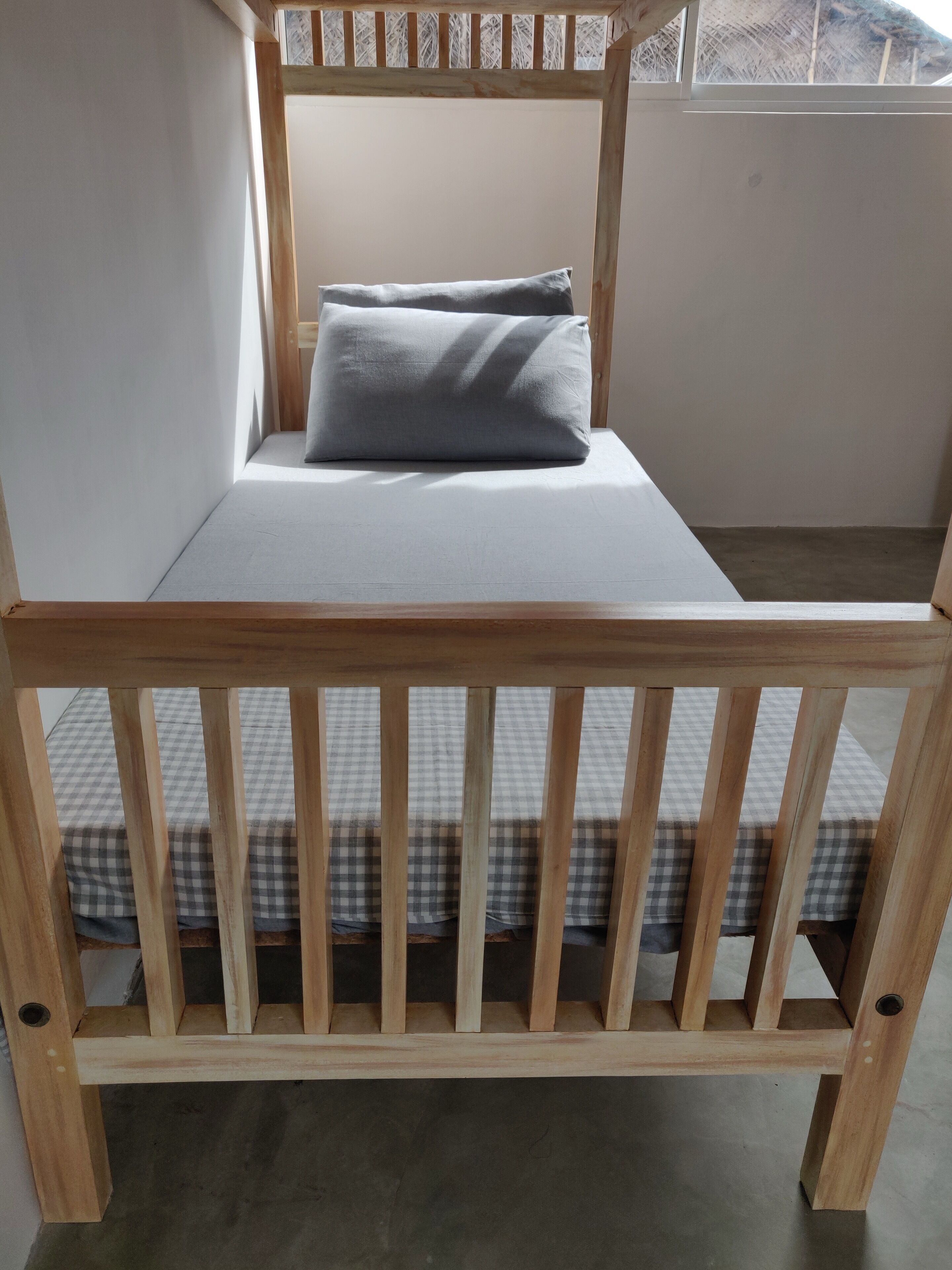 Un lit superposé en bois, avec un matelas à carreaux en bas et un lit simple avec un oreiller gris en haut.