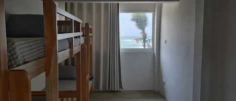 Una habitación con literas, una ventana con cortinas y vista al mar.