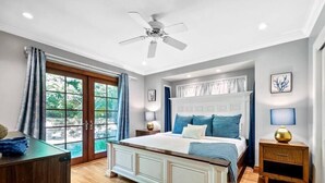 Ein Schlafzimmer mit einem großen Bett, Holzboden, Deckenventilator und Blick durch eine Glastür.