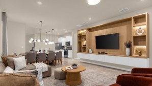 Een moderne woonkamer met een bank, voetenbankje, salontafel en een rode fauteuil. Op de achtergrond is een eethoek met stoelen en een tafel te zien.