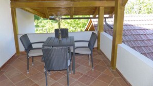 En overdækket terrasse med træloft, et bord, fire stole og en vase med blomster.