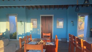 A dining area with a wooden table and chairs, a sofa, and a door. - 3bd 2 bth House. POOL! HOTTUB! Breathtaking Ocean Views! 2-min drive to beach! (Santos Guardiola)