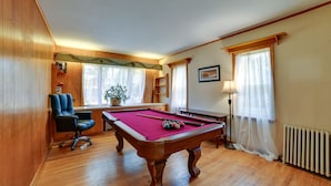 Uma mesa de bilhar em um ambiente com paredes de madeira e uma janela.