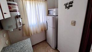 Cocina compacta con termo, refrigerador, microondas y un cartel de café en la pared.
