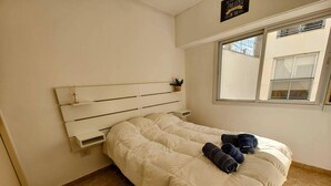 Una cama bien tendida con un cabecero blanco y una pequeña planta en maceta sobre la repisa.
