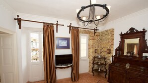 A room with a brick wall, a wooden dresser, a chandelier, and a television. - Galiello & Bacco by CorfuEscapes (Corfu)