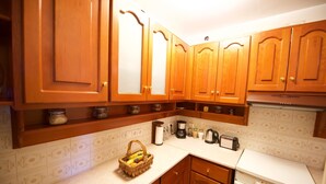 A kitchen with wooden cabinets, a countertop, a toaster, a coffee maker, and a basket of bananas. - Galiello & Bacco by CorfuEscapes (Corfu)
