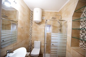 Une salle de bain équipée de toilettes, d’une douche et d’un espace de douche clos par des parois en verre.