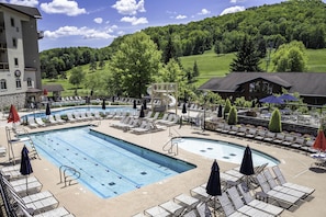 A pool area with lounge chairs, a water slide, and a view of a green landscape. - SnowPine Condo, King Bed, 2 Full Baths (Ellicottville)