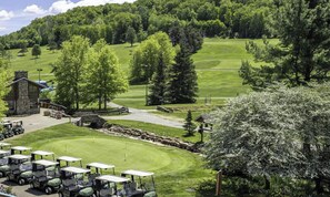 A golf course with a clubhouse, a parking area with golf carts, and surrounding greenery.