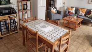 A cozy living room with a tiled floor, wooden furniture, a coffee machine, a refrigerator, and a sofa with decorative pillows. - Le Gîte du Tilleul (Pernes-les-Fontaines)