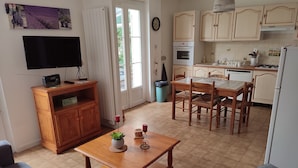 A compact kitchen with a dining area, wooden furniture, and a TV on a stand. - Le Gîte du Tilleul (Pernes-les-Fontaines)