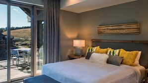 Un dormitorio moderno con una cama grande, una mesita de noche, una lámpara y vistas a un balcón con mobiliario exterior.