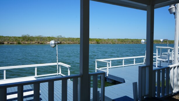 A covered dock with white railings and a clear view of the water and distant shoreline. - Sunshine cabin with a Shared fishing pier Not waterfront (Rio Hondo)