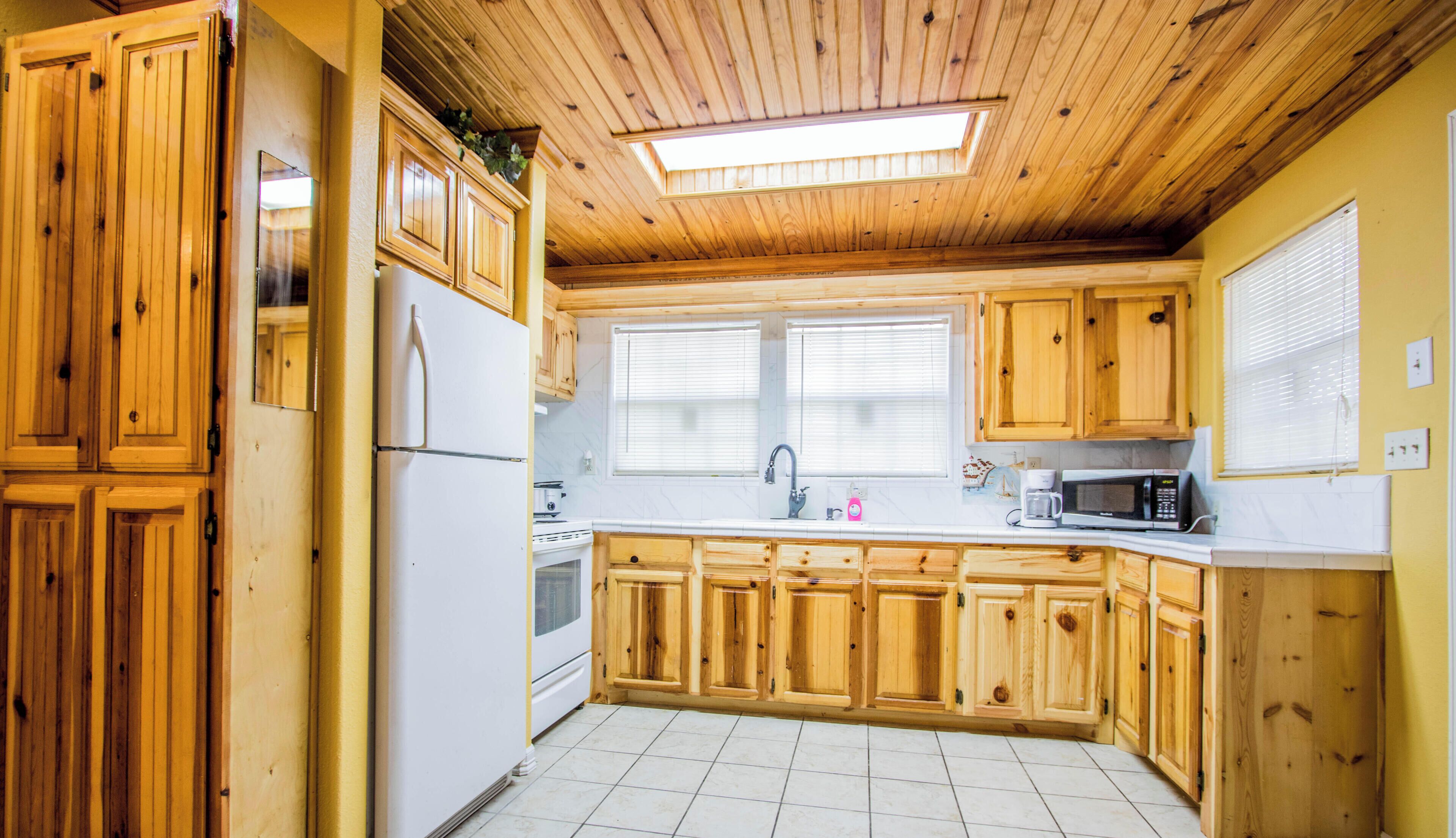 Une cuisine avec des meubles en bois, un réfrigérateur, un four à micro-ondes et une fenêtre avec des stores.