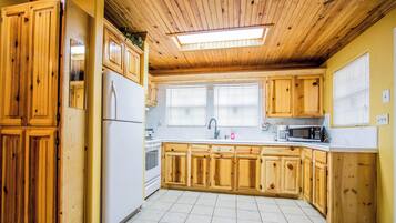 A kitchen with wooden cabinets, a refrigerator, a microwave, and a window with blinds.