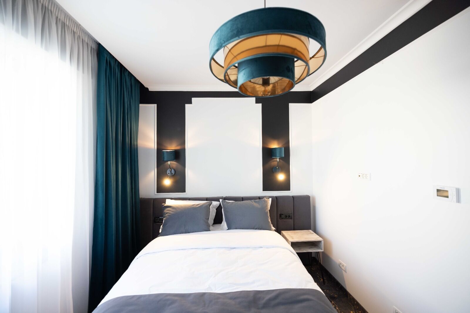 Una habitación de hotel moderna con una cama grande, dos mesitas de noche, una lámpara de pared y una lámpara del techo.