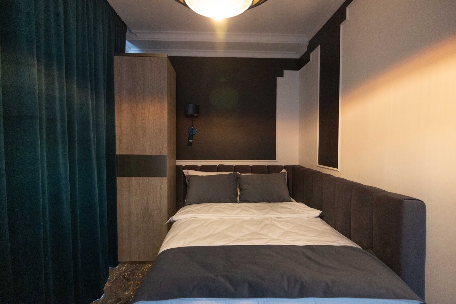 A compact hotel room with a single bed, dark wood headboard, and a ceiling light fixture.