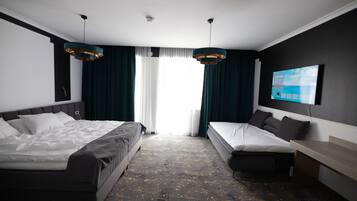 Habitación de hotel con dos camas, un televisor montado en la pared y un ventanal con cortinas.