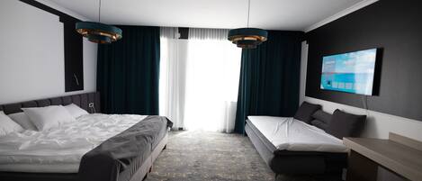 A hotel room with two beds, a TV mounted on the wall, and a large window with curtains.