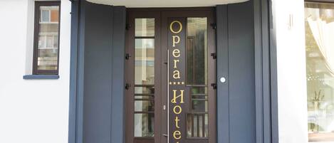 A hotel entrance with a dark brown door, a glass panel, and the name "Opera Hotel" in gold lettering.