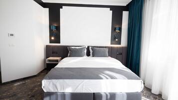 A modern hotel room with a large bed, two bedside tables, a wall-mounted TV, and a dark-colored curtain.