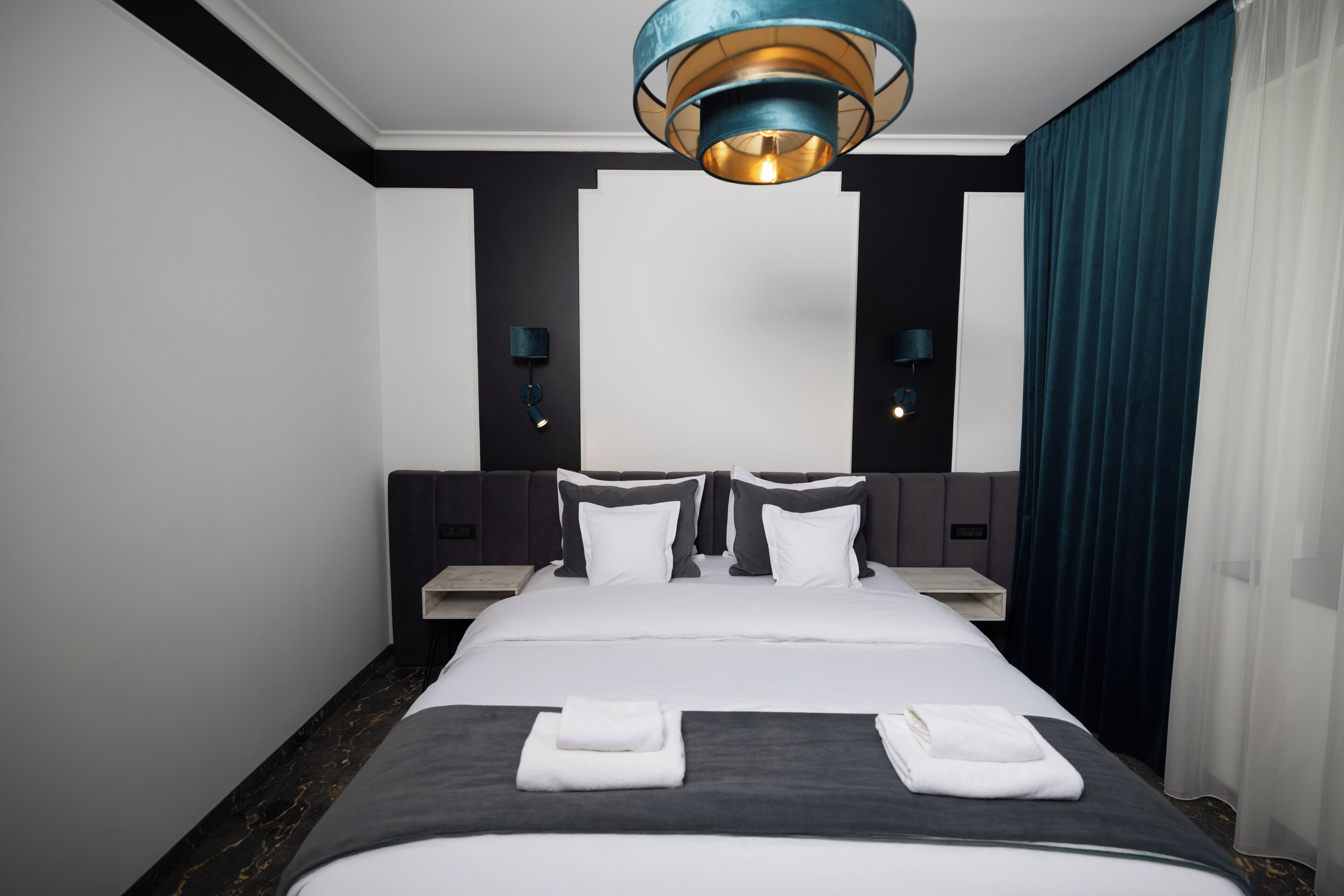 A hotel room with a large bed, two bedside tables, a modern chandelier, and a view of the city.