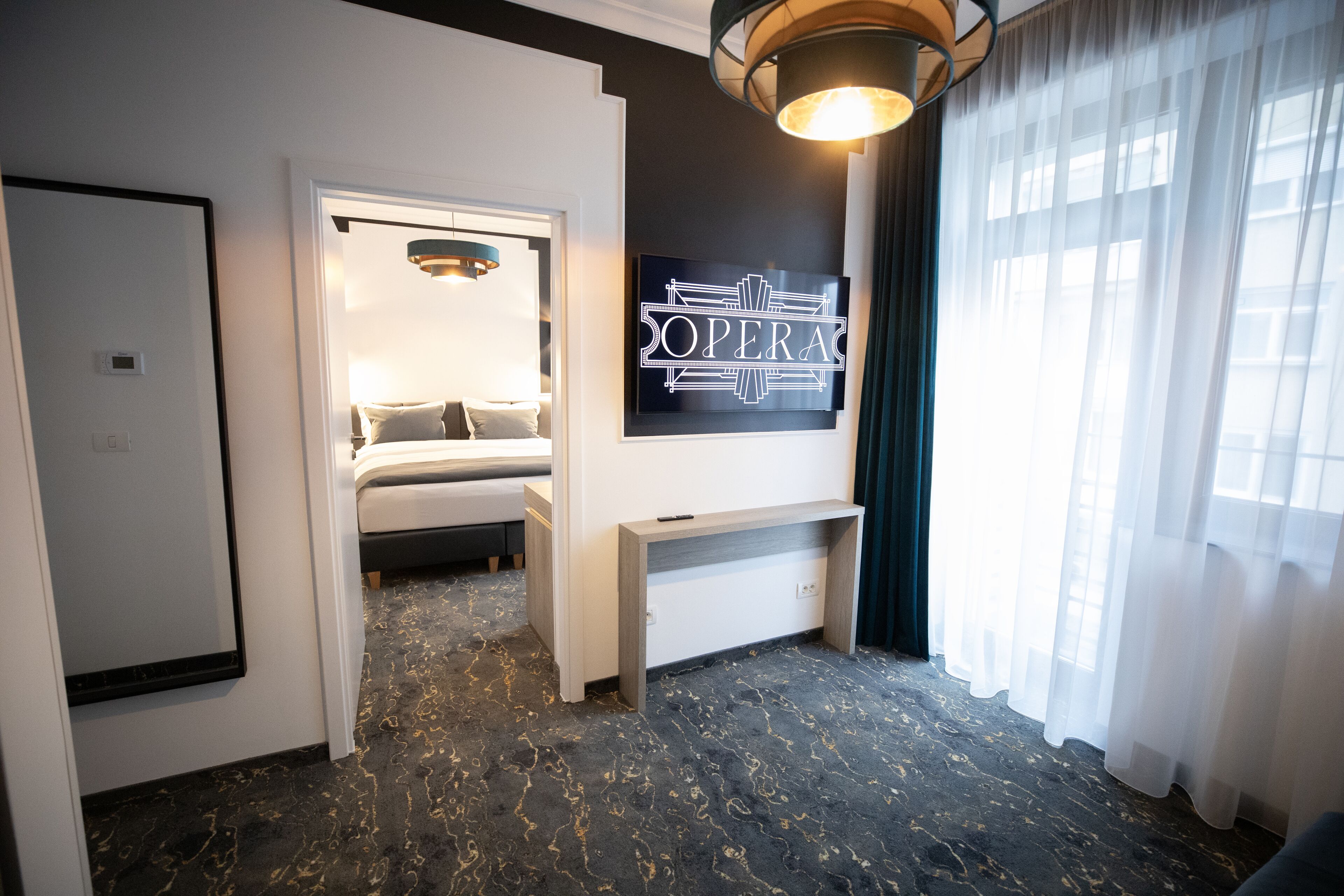 Une chambre d’hôtel avec un lit, un bureau, un panneau fixé au mur et une grande fenêtre avec des rideaux.
