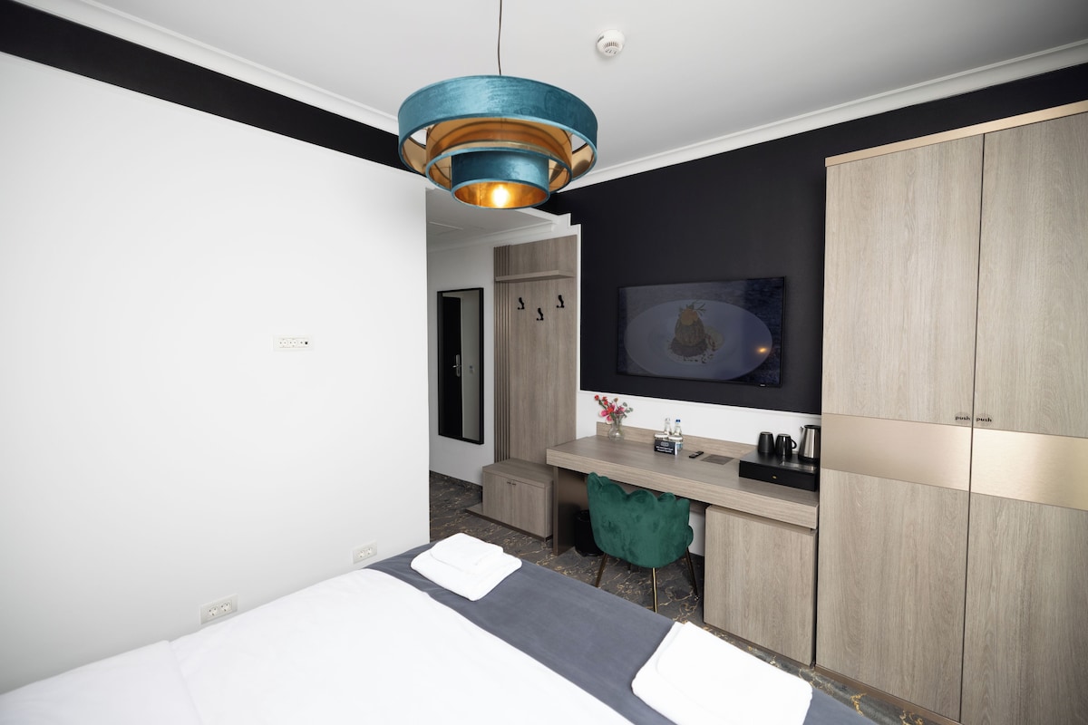 A modern hotel room with a bed, a desk, a wardrobe, and a pendant light.