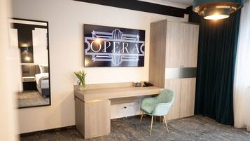 A modern hotel room with a wooden desk, a green chair, a large mirror, and a sign that reads "OPERA".