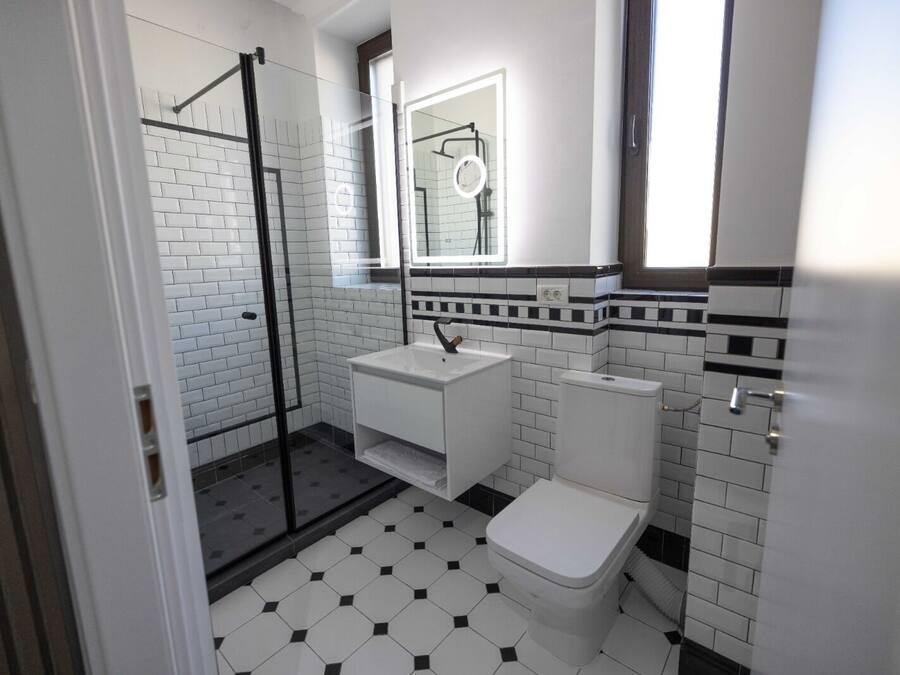 A bathroom with a glass shower enclosure, a white sink, a toilet, and a tiled floor.