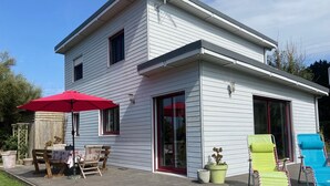 Een tweelaags huis met een terras, een patio met een tafel en stoelen, en twee lounge fauteuils.