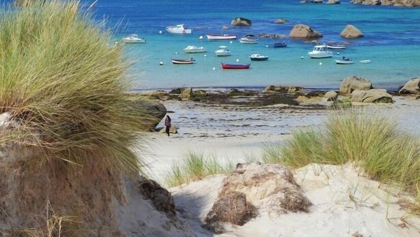 Een strand met boten, helder water en rotsformaties.