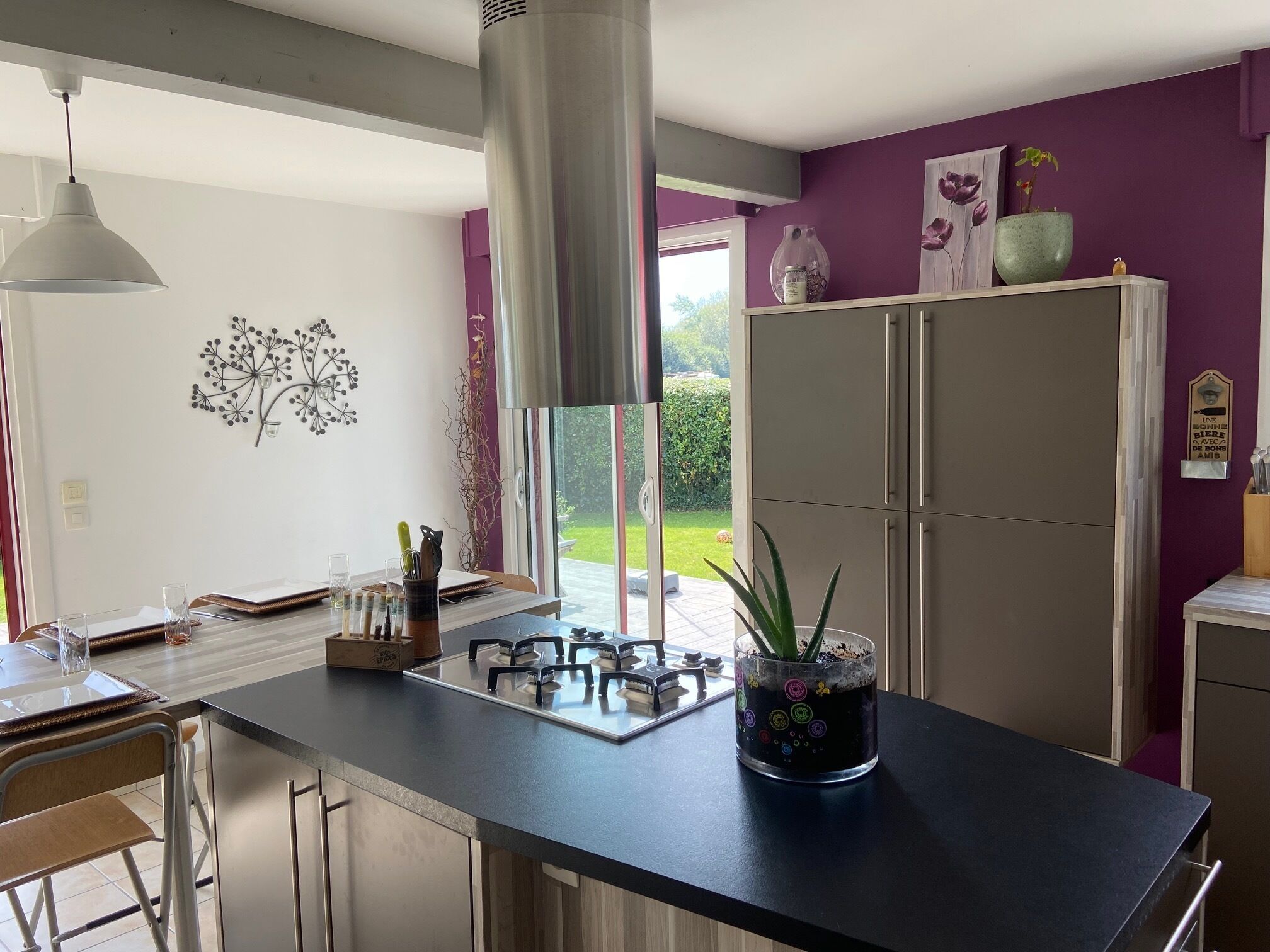 Een moderne keuken met een centraal eiland, roestvrijstalen apparatuur en uitzicht op de tuin door grote ramen.