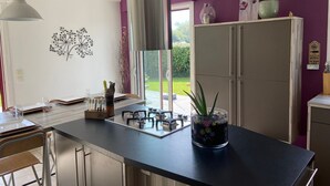 Een moderne keuken met een centraal eiland, roestvrijstalen apparatuur en uitzicht op de tuin door grote ramen.